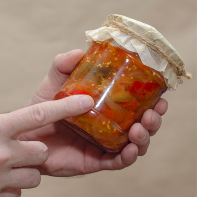 botulismo La persona tiene un barattolo di verdure sottaceto nella mano sinistra e ne indica il contenuto con l'indice destro