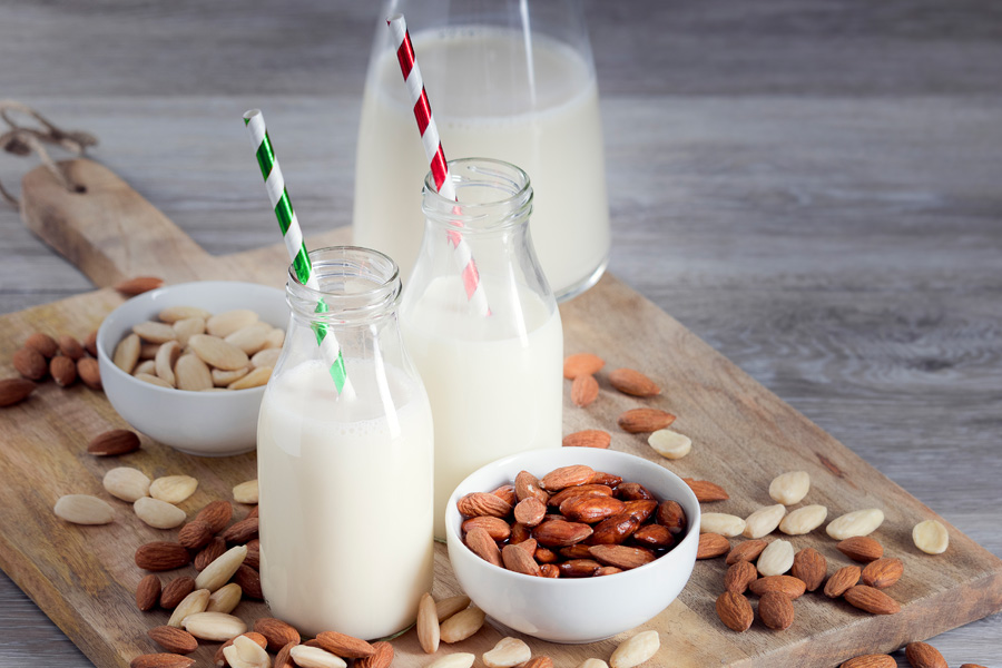 Ricetta per cocktail analcolico alle mandorle Immagine d'atmosfera "cocktail di mandorle analcolico": due bottiglie a collo largo riempite con cannucce colorate sono appoggiate su una tavola di legno con mandorle