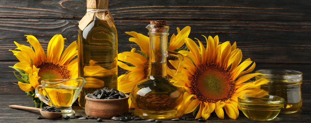 Guida alla produzione dell'olio Immagine d'atmosfera "Produzione di olio": olio di girasole in bottiglie disposte con girasoli e semi di girasole su uno sfondo di legno