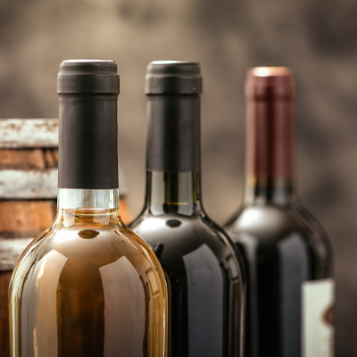 Guida alla classificazione dei vini Immagine d'atmosfera "Classificazione del vino": tre bottiglie di vino sono disposte una dietro l'altra davanti a una botte di legno marrone