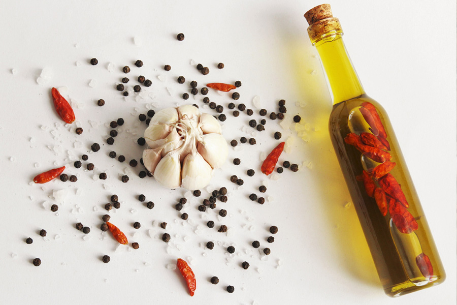 Immagine d'atmosfera: una bottiglia di olio al peperoncino è accanto a spezie come aglio, peperoncino, sale e pepe