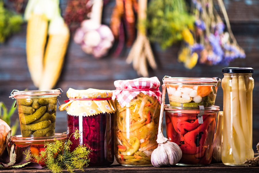 Verdure sott'aceto Gruppo di barattoli con verdure sottaceto disposti davanti a una parete con verdure essiccate