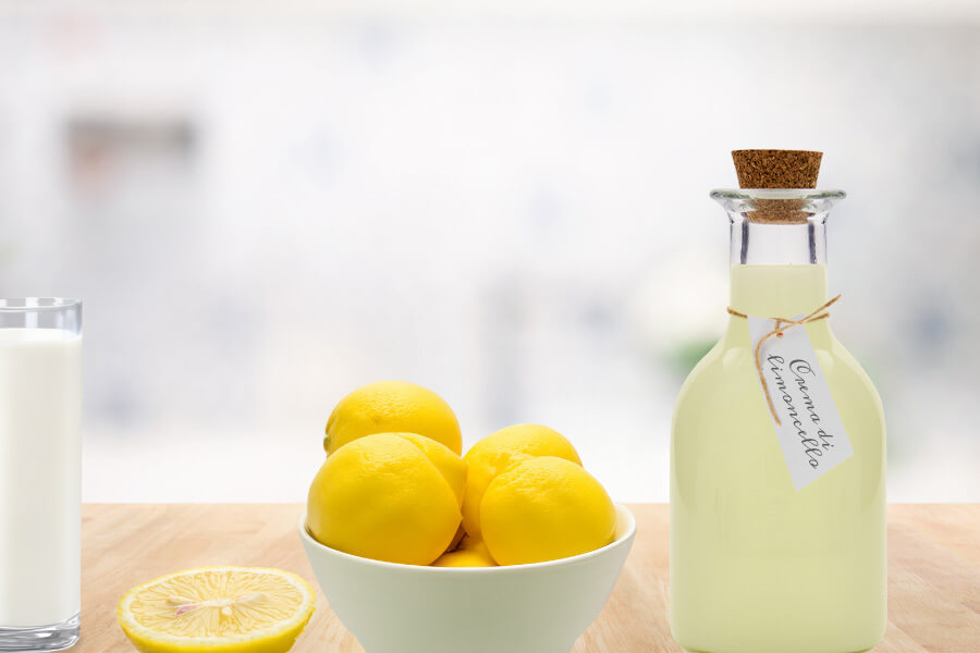 Crema al limoncello Immagine d'atmosfera: bottiglia con crema di limoncello disposta con una ciotola di limoni e un bicchiere di latte