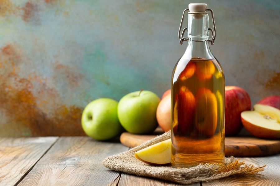 Bottiglia di aceto di mele riempita Immagine d'atmosfera: una bottiglia di aceto di mele su un tavolo di legno, con delle mele drappeggiate intorno