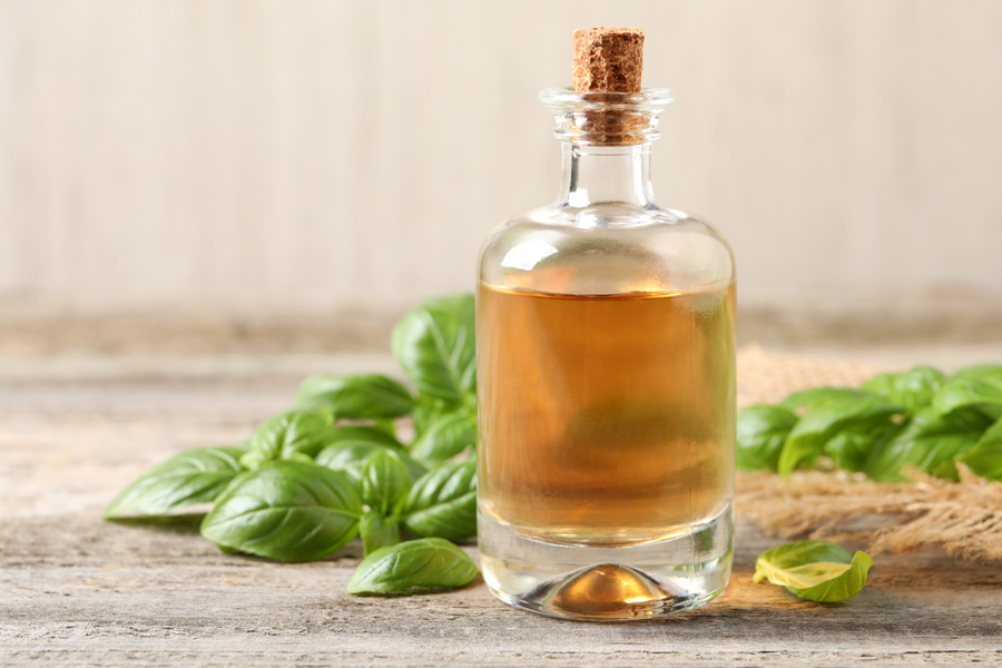 Ricetta dell'olio al basilico Immagine d'atmosfera: una bottiglia di sughero è piena di olio e circondata da basilico