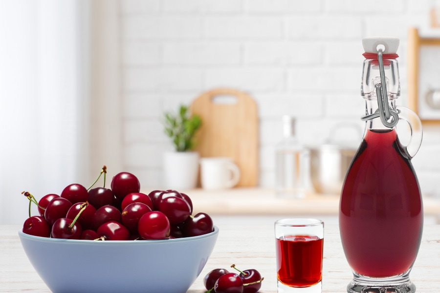 Liquore alle ciliegie: una ricetta facile e gustosa Immagine d'atmosfera: una bottiglia di liquore è riempita e circondata da ciliegie