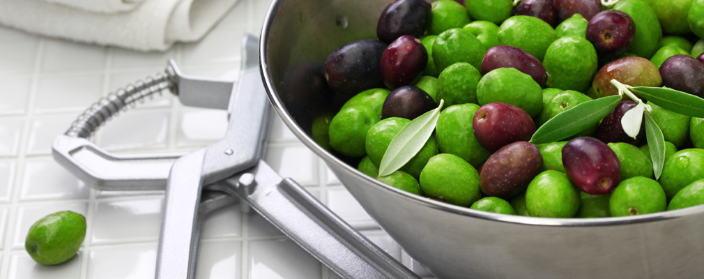 Una ciotola piena di olive e uno snocciolatore per le olive in modo che possano essere ulteriormente lavorate