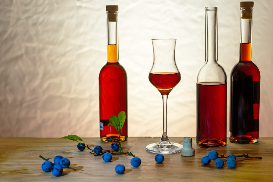 Ricetta del liquore al mirto Immagine della ricetta Liquore al mirto: tre bottiglie di sughero riempite di liquore al mirto, tra un bicchiere pieno e rumoroso, disposte con bacche di mirto in una luce soffusa