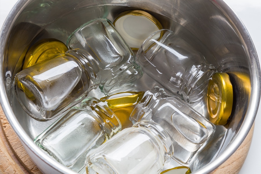 Immagine di ispirazione per la guida alla sterilizzazione dei barattoli: i barattoli twist-off e i coperchi vengono posizionati in una pentola di acqua calda