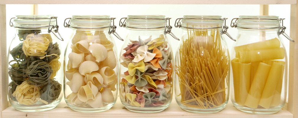 Striscione con barattoli con cornice in filo metallico in fila uno accanto all'altro, riempiti con diversi tipi di pasta